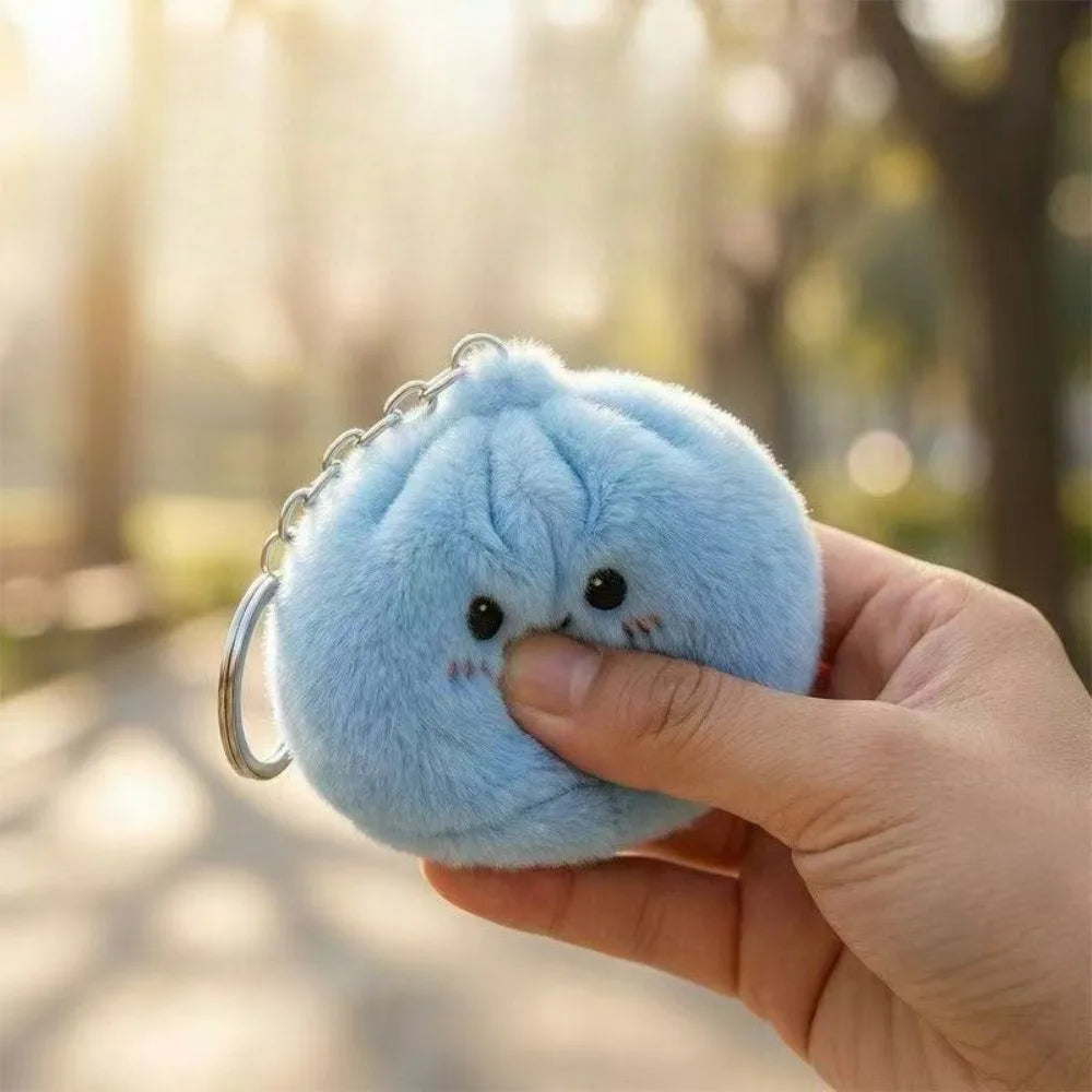 A hand holds a light blue squishy dumpling keychain plush against a blurred outdoor background.