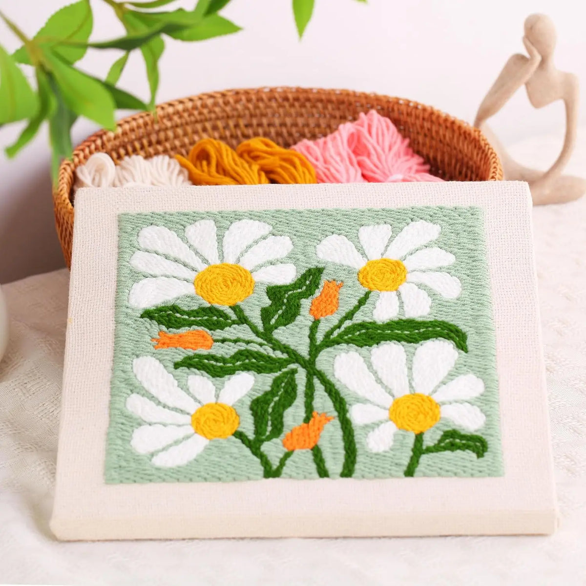 A punch needle embroidery kit featuring a white and yellow daisy flower pattern on a light green fabric.