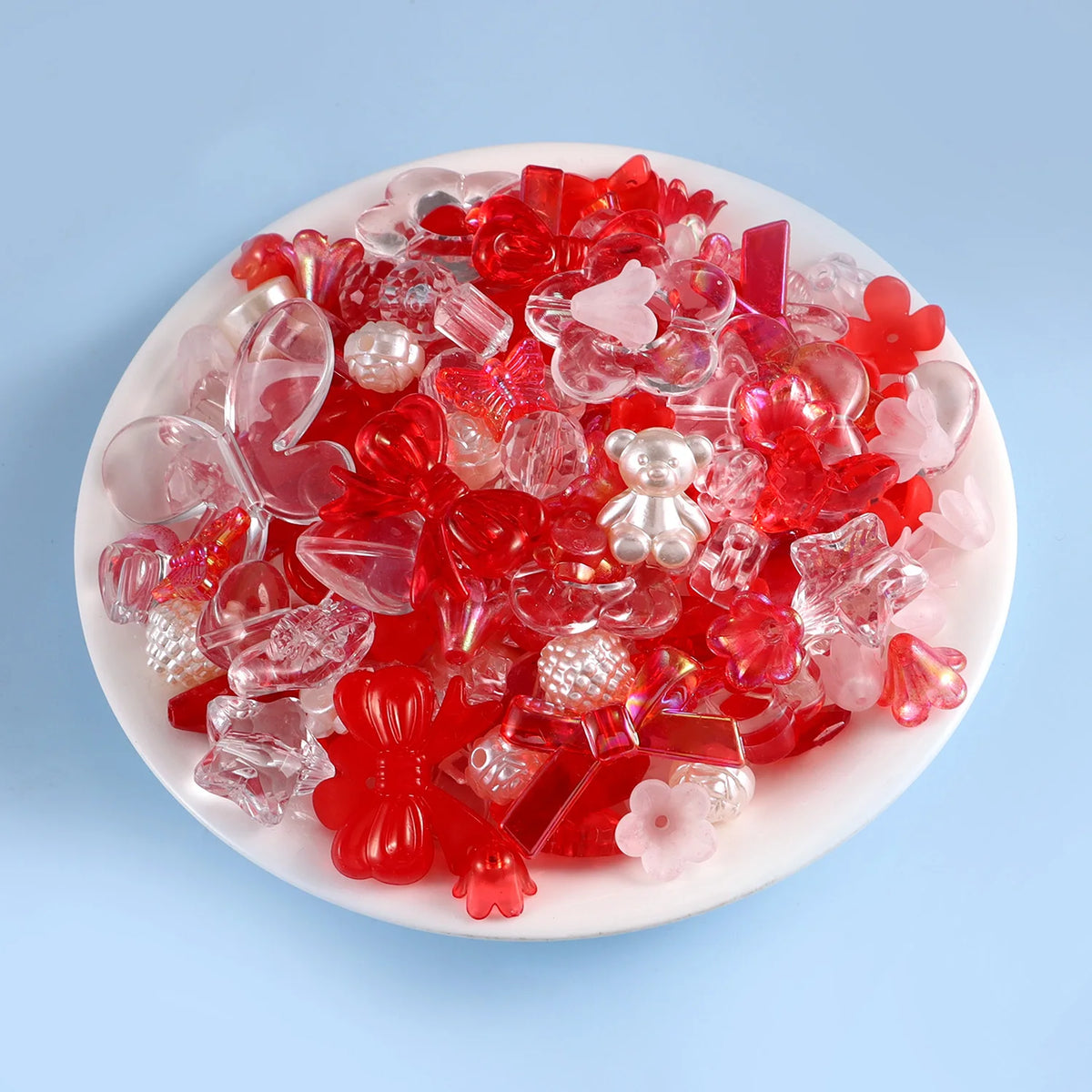 A mix of red and pink acrylic beads for DIY jewelry making, including various shapes like hearts and teardrops.