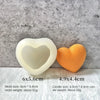 A white silicone heart mold and an orange candle are displayed on a gray textured background.