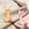A pair of silicone teether toys, one yellow and one pink, resting on a light fabric.