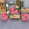 A miniature doll sofa set with a red and white checkered fabric, a doll, and wooden furniture.