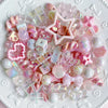 A collection of pink and iridescent acrylic bow and flower beads scattered on a white surface.