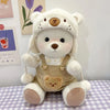 A white teddy bear plush doll wearing beige overalls and a headband, sitting on a checkered surface.