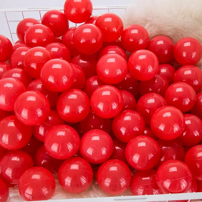 A bulk set of bright red plastic ocean ball pit toys piled in a white crate.