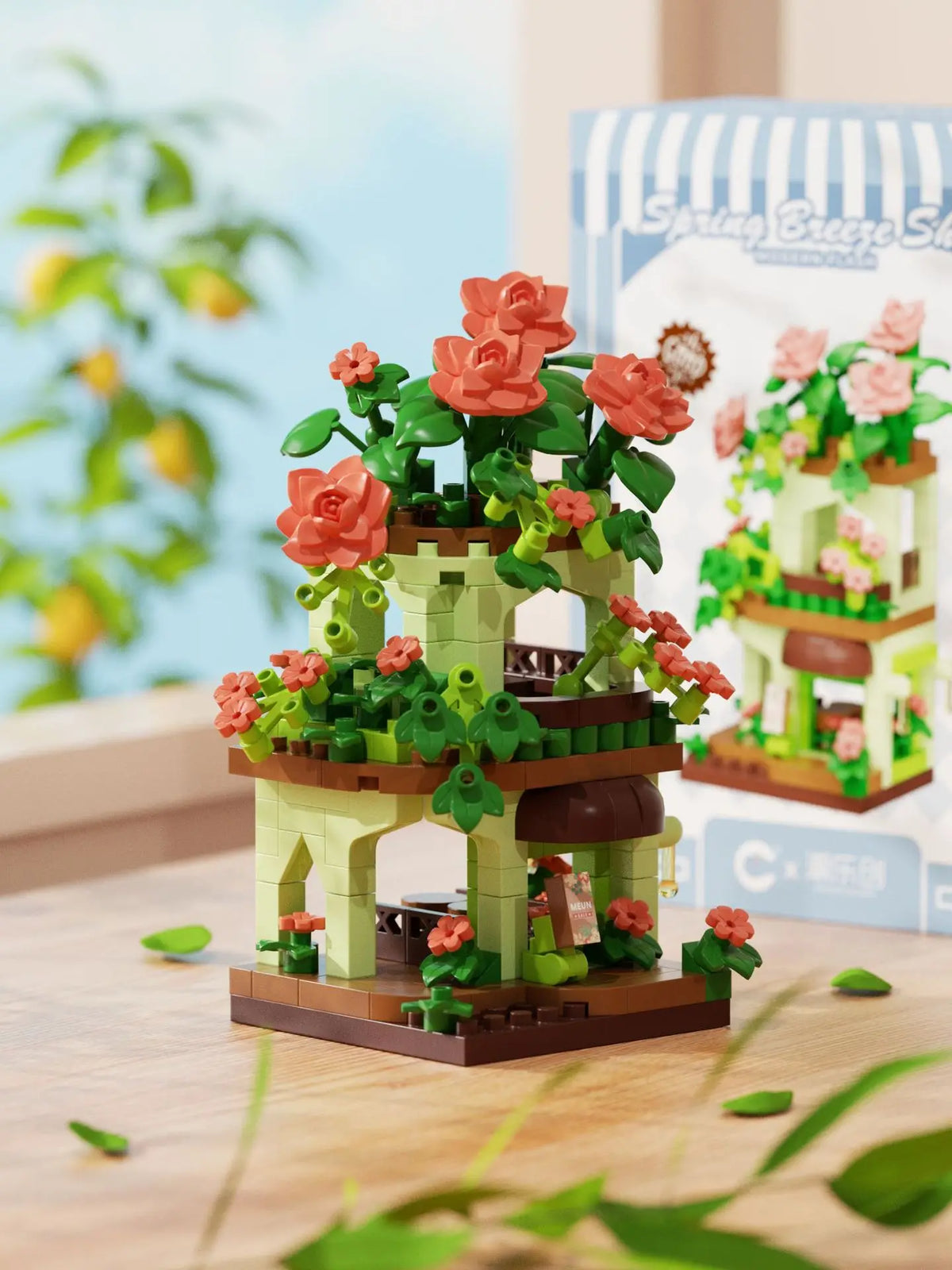 A miniature building set featuring a green woodland cabin with orange roses and pink flowers, displayed on a wooden surface.
