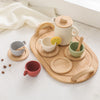 A wooden pretend play tea party set featuring cups, saucers, and a teapot arranged on a wooden serving board.