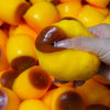 A hand is squeezing a yellow caramel pudding squishy stress relief ball, showing the soft texture and color variation.