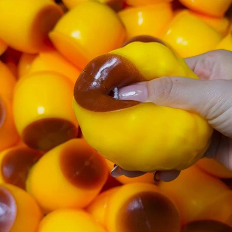 A hand is squeezing a yellow caramel pudding squishy stress relief ball, showing the soft texture and color variation.
