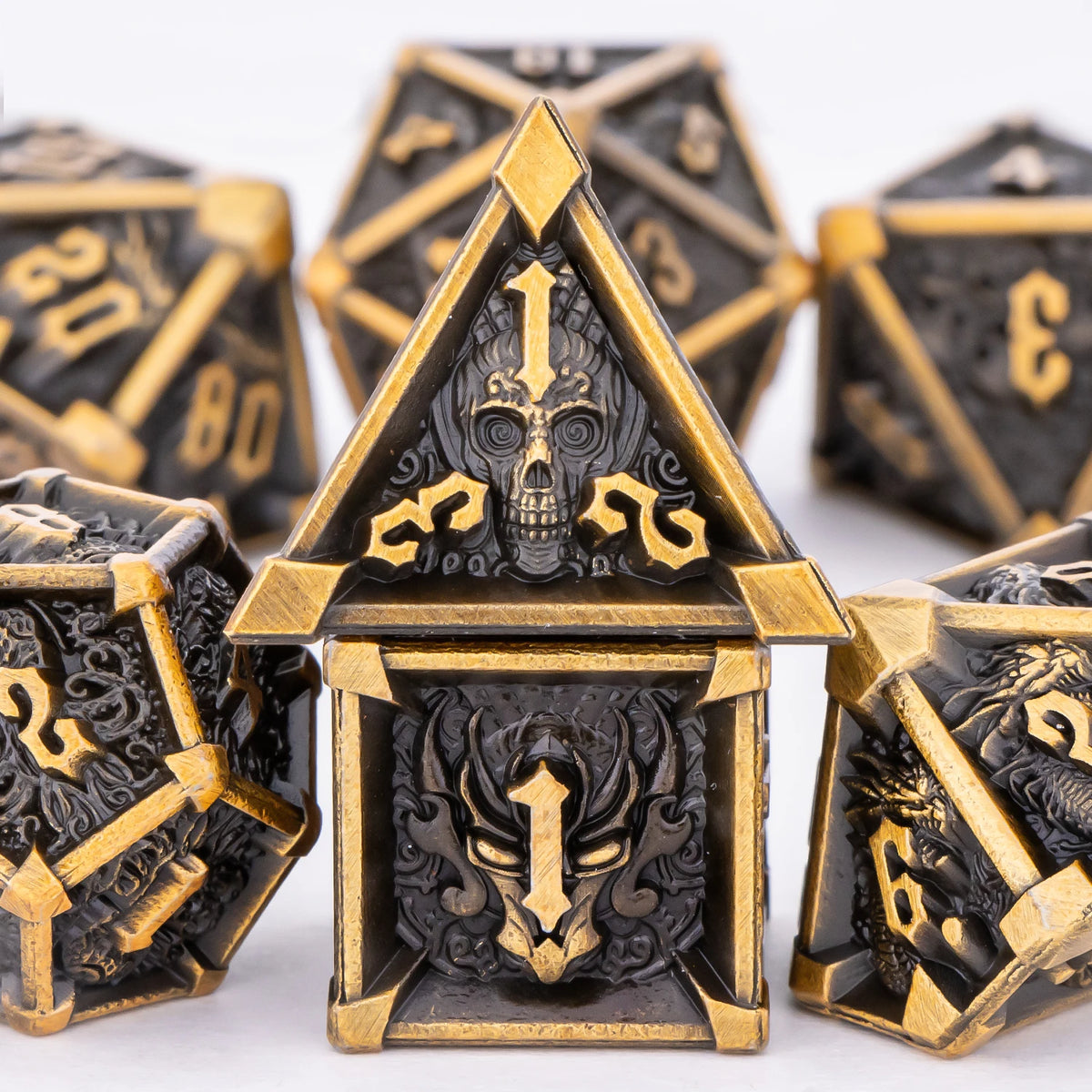A close-up of a gold and black metal dice set featuring skull and dragon designs for tabletop role-playing games.