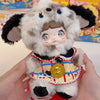 A fluffy white and black collectible doll with large eyes and a gold medallion is held in a person's hands.