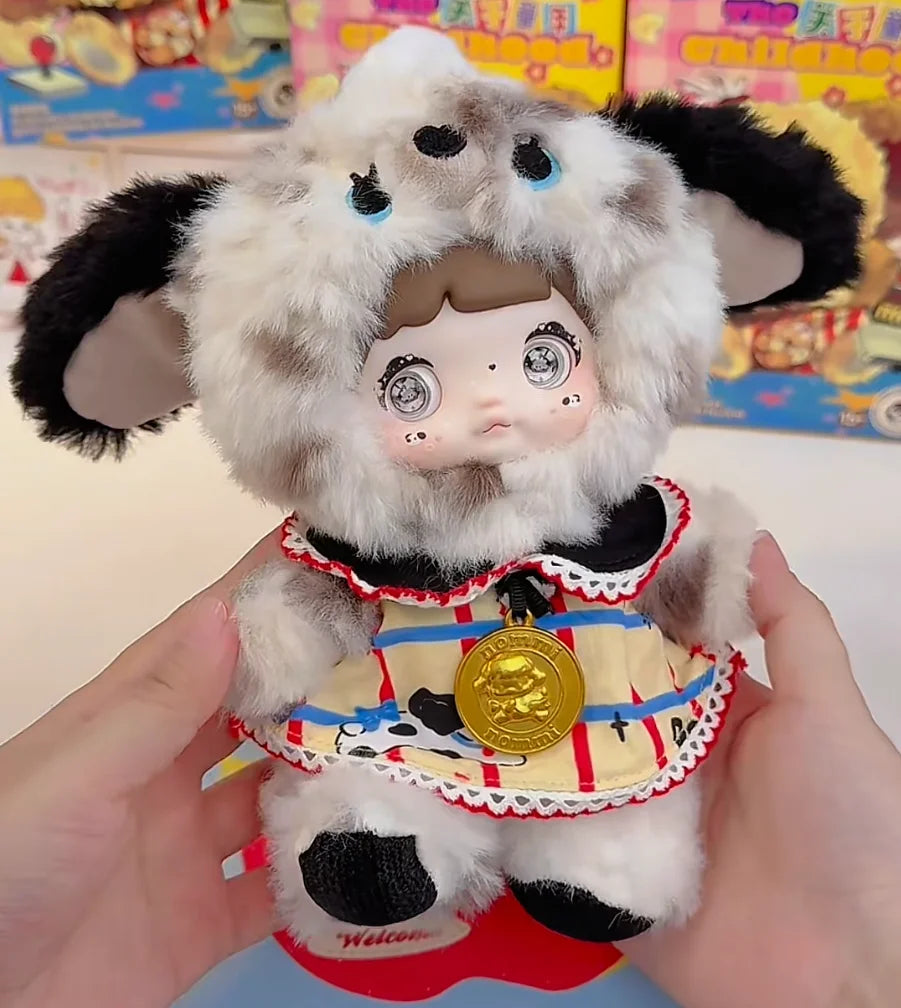 A fluffy white and black collectible doll with large eyes and a gold medallion is held in a person's hands.