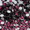 A close-up view of various flatback glass crystal rhinestones in shades of pink, red, and black on a white background.