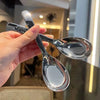 A hand holds a clear glass spoon and fork set against a blurred indoor background.