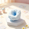 A light blue squishy sensory stress ball fidget toy resting on a white block with colorful star-shaped tiles in the backgroun
