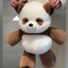 A fluffy white and brown panda stuffed animal being held by two hands.