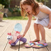 A young girl is playing with a pink ant-shaped water blaster toy on a wooden floor.