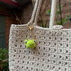 A light beige crocheted bag with a gold-colored keychain featuring a small green rabbit or chick charm.