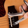 A hand holds a silver guitar capo clamp, positioned over the strings of a guitar.