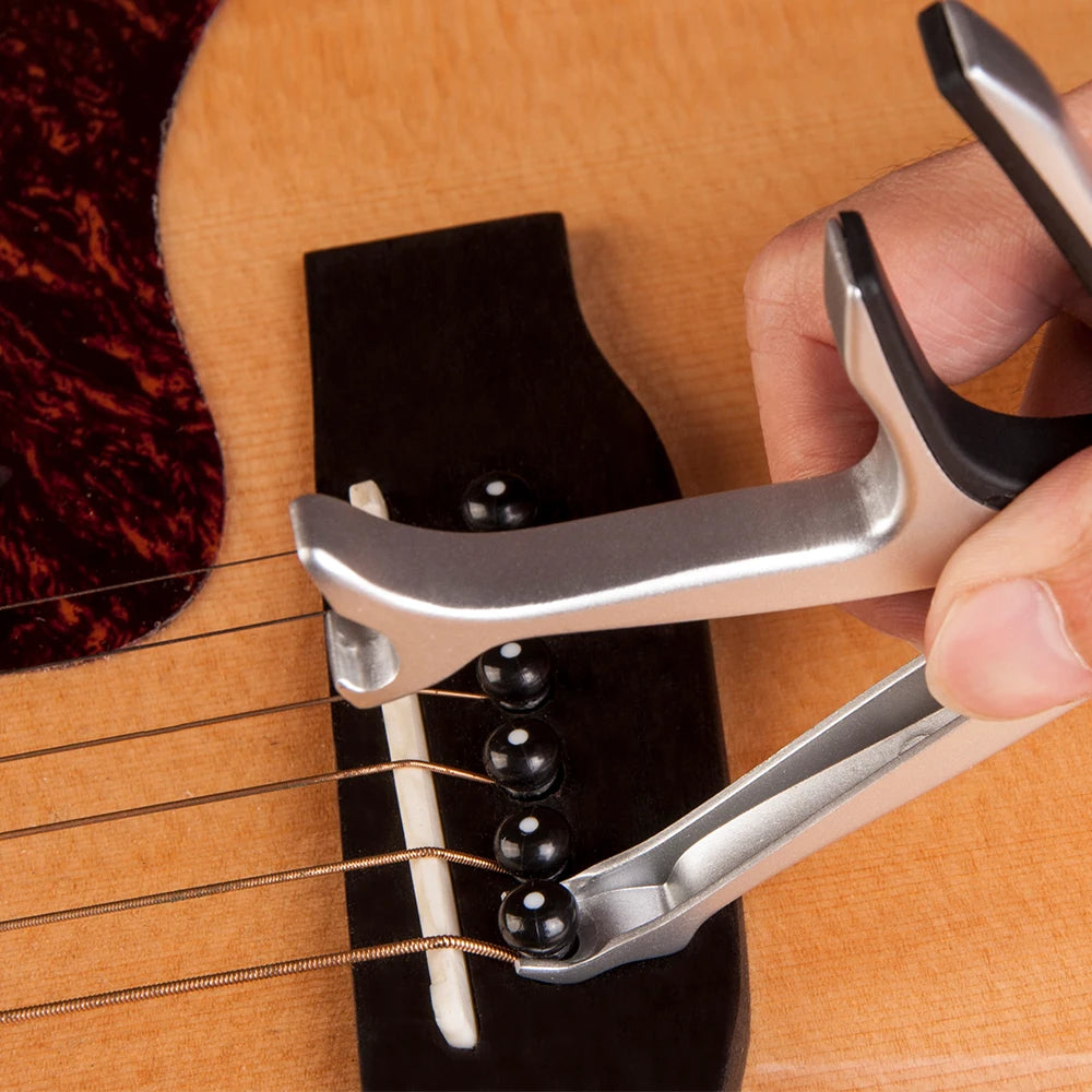 A hand holds a silver guitar capo clamp, positioned over the strings of a guitar.