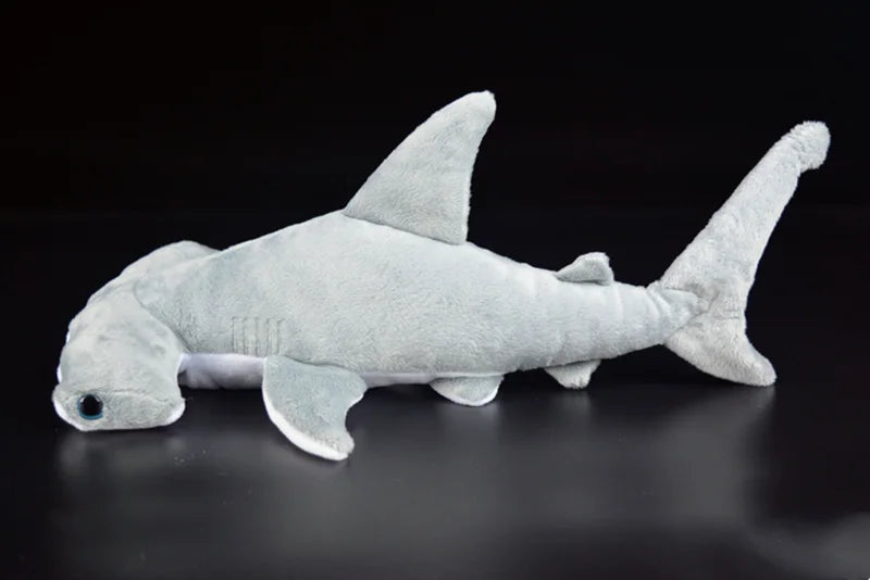 A light gray super soft hammerhead shark plush toy lying on a dark surface.