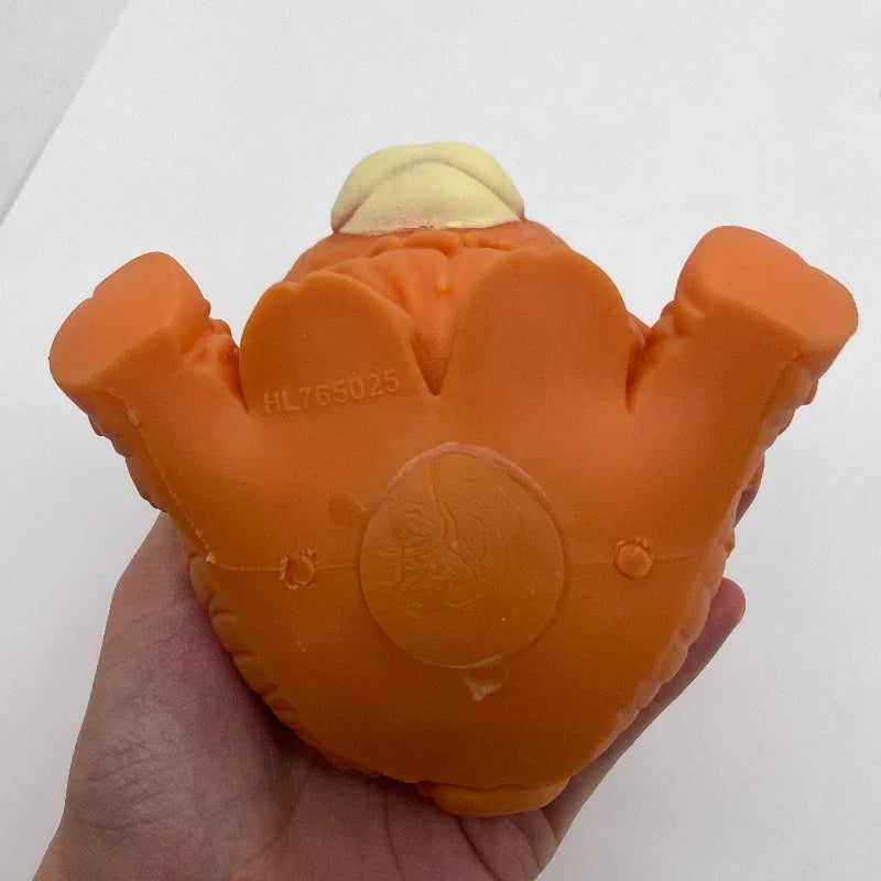 An orange squishy stress ball shaped like a Highland cow head with a yellow tuft, held in a hand.