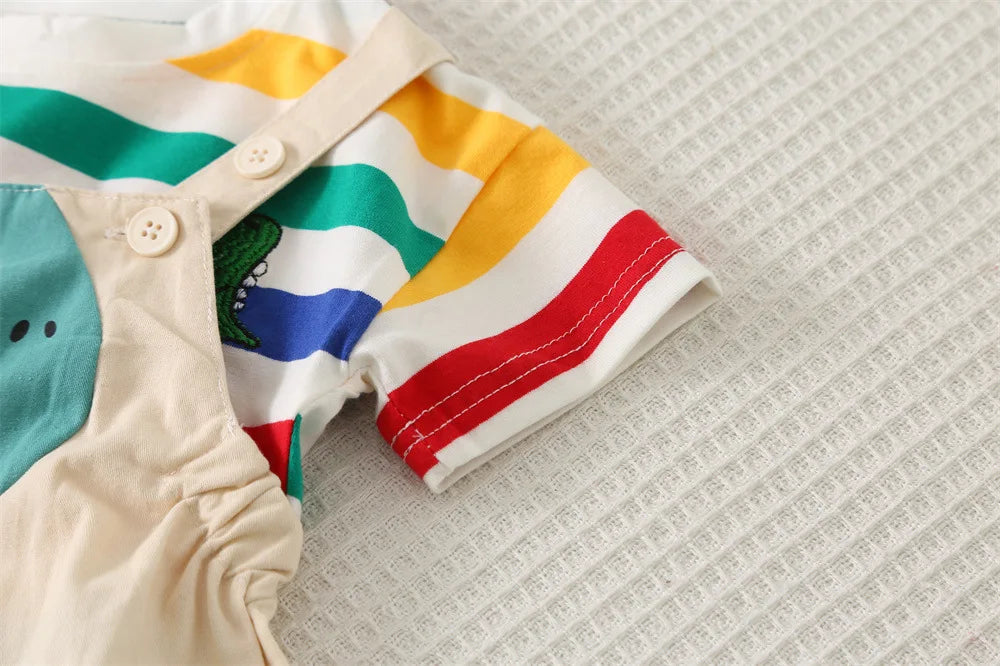 A close-up of a kids' striped dinosaur two-piece outfit set featuring yellow, green, and blue stripes on a light fabric.