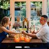 A woman and a man are holding hands over a wooden table with candles and greenery in a bright room.