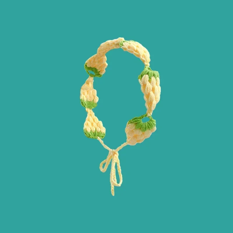 A handmade strawberry crochet headband with a wide elastic band against a teal background.