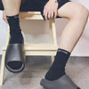 A person wearing black socks and grey EVA platform slides is sitting on a wooden stool.