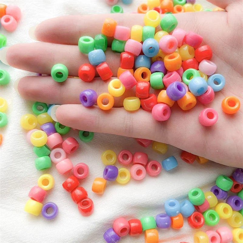 A hand holds a large collection of colorful pony beads in various shades of pink, orange, yellow, green, and purple.