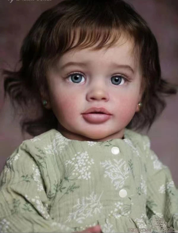 A close-up portrait of a realistic reborn baby doll named Pippa with blue eyes and brown hair wearing a light green patterned