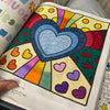 A colorful coloring page featuring a heart design surrounded by radiating rainbow patterns and various colored shapes.