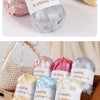 A collection of nine colored satin ribbon yarn skeins displayed in an open wooden box.