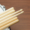 A set of light wood maple drumsticks resting on a metal stand.