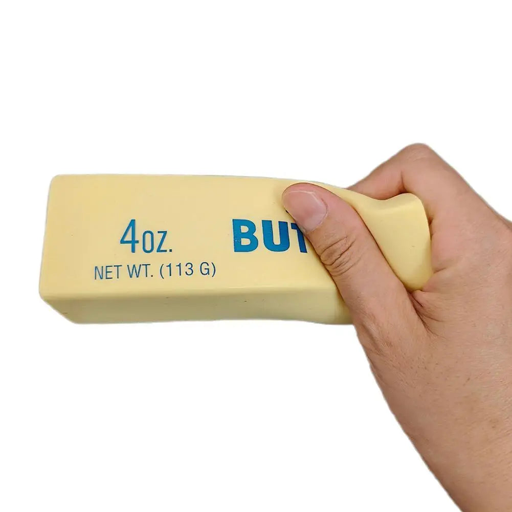 A hand holds a yellow squishy butter stick fidget toy with '4oz' and 'BUT' markings on it.
