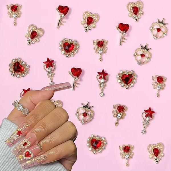 A hand displays various 3D red love heart nail art charms and gold keys on a pink background.