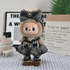 A plush Labubu doll wearing a black and gray flannel outfit with a bow and a flower, displayed in front of a sign.