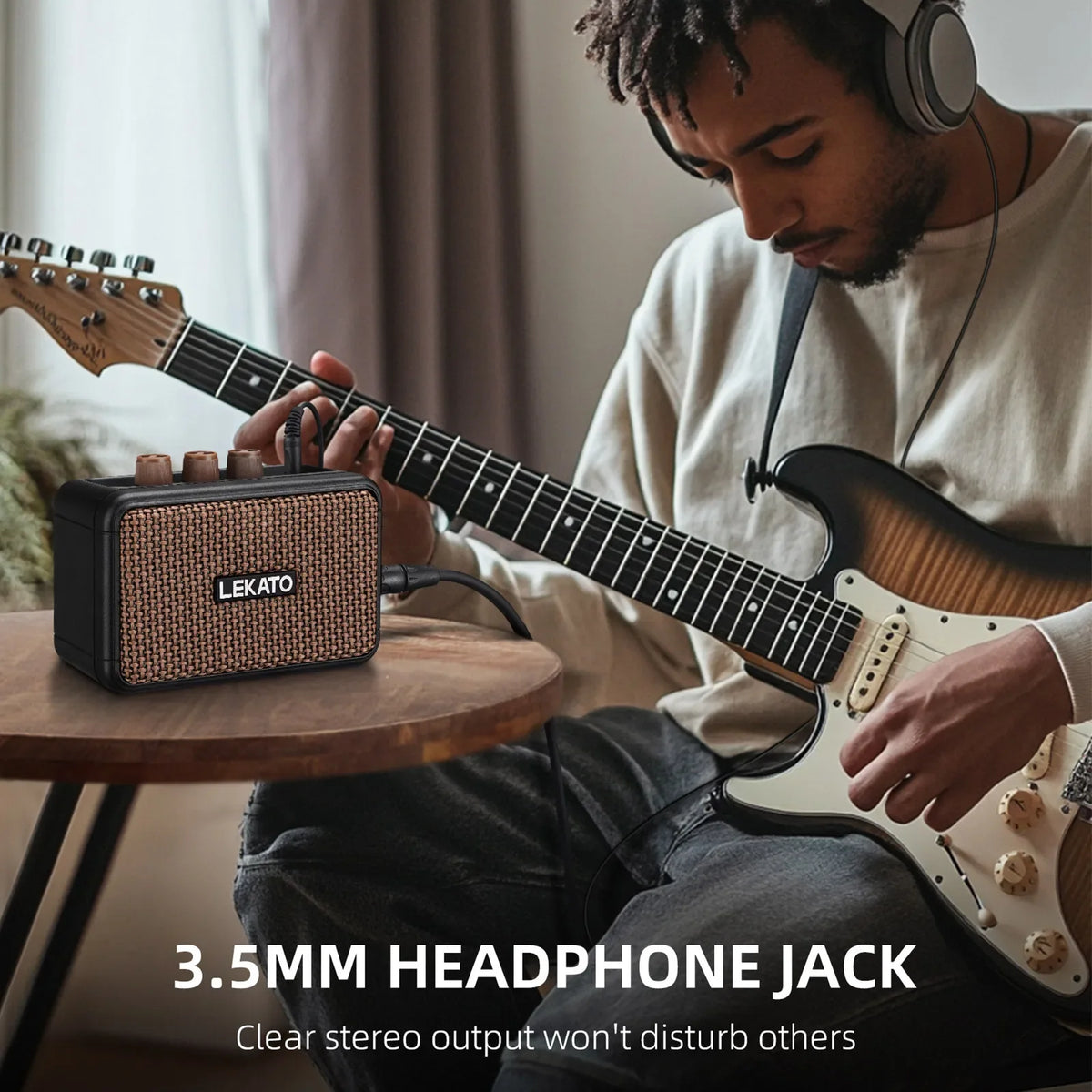 A man plays an electric guitar with a Lekato amplifier and headphones in a softly lit indoor setting.