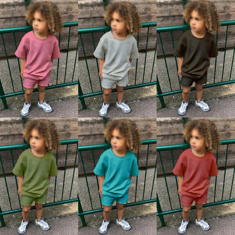 A young child wearing a pink short sleeve top and shorts standing outdoors.