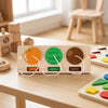 A wooden Montessori busy board featuring orange, watermelon, and kiwi fruit sections for sensory play.