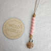 A string of pink wooden beads attached to a leather cord and a silicone clip on a white background.