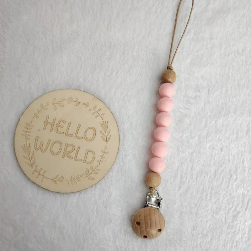 A string of pink wooden beads attached to a leather cord and a silicone clip on a white background.