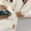 A close-up of a cream fleece jacket and pants set featuring brown bear cartoon prints with green accents.