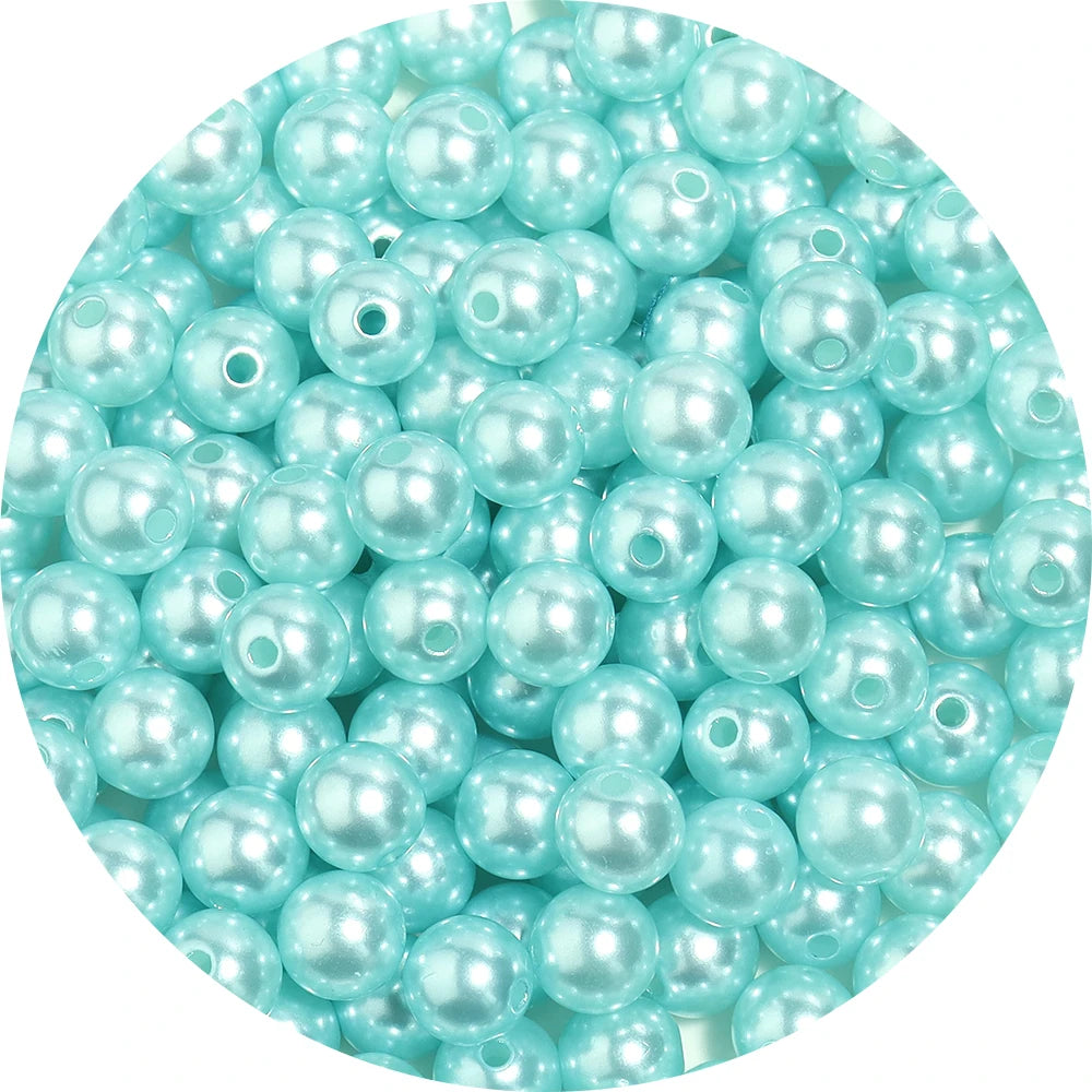 A close-up view of small, light blue imitation pearl beads scattered in a pile.