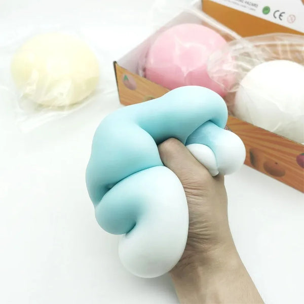 Une main serre une boule anti-stress géante bleu clair à côté de squishies roses et blancs.
