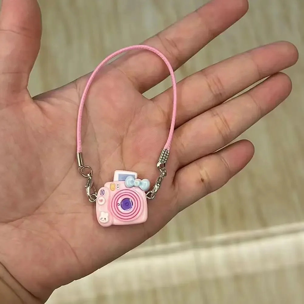 A pink beaded necklace with a small camera doll charm is held in a hand.