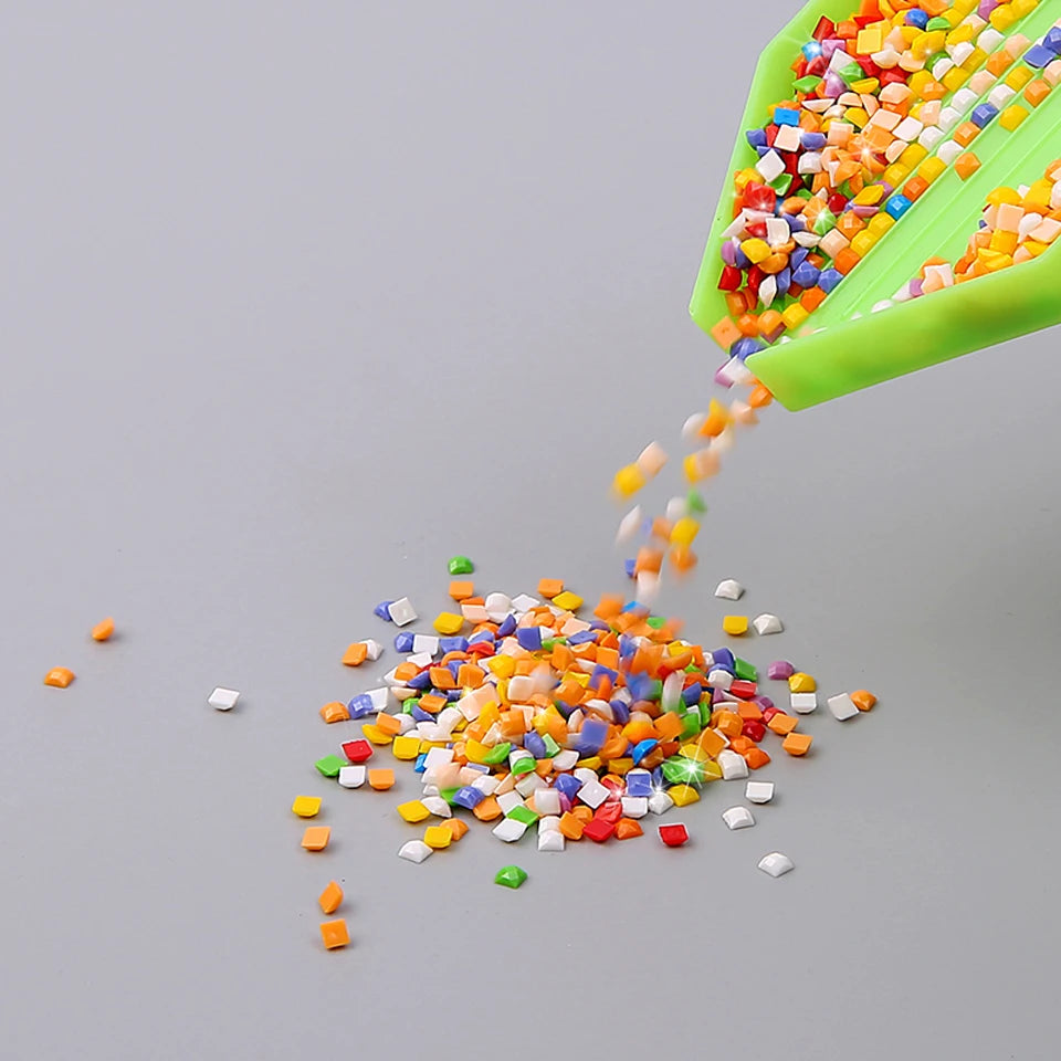 A green scoop is pouring colorful sequins and glitter onto a gray surface.