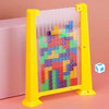 A clear plastic puzzle box filled with colorful building blocks is displayed in front of a pink surface.