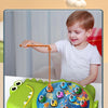 A young boy is playing with a green magnetic fishing toy set, attempting to catch orange fish on a string.